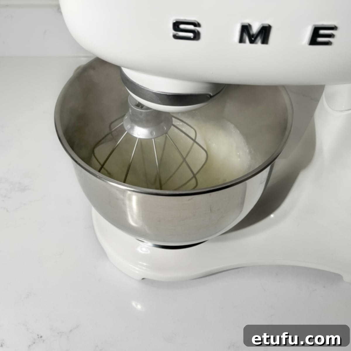 The Swiss meringue whipping in a stand mixer, gradually increasing in volume and becoming glossy.