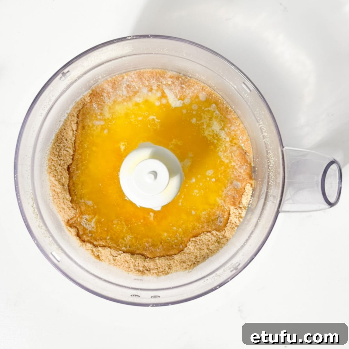 Melted butter being added to biscuit crumbs in a food processor, ready to be mixed.