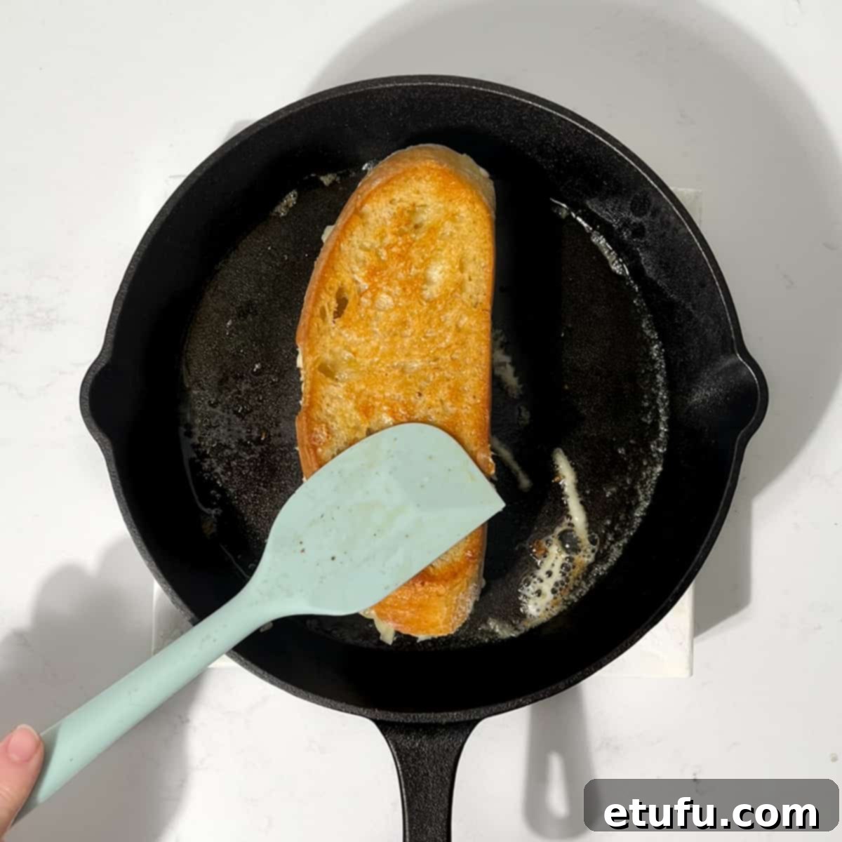 Flipping the sourdough grilled cheese sandwich in a cast iron pan.