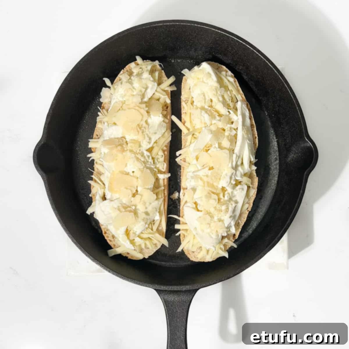 Adding tow slices of bread topped with cheese to a cast iron skillet.