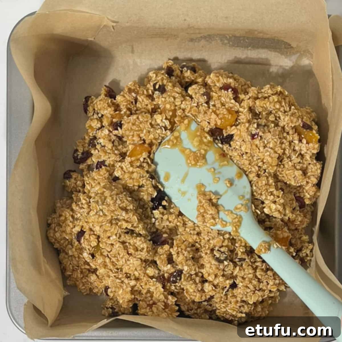 Pressing the flapjack mixture into a square, lined baking tin.