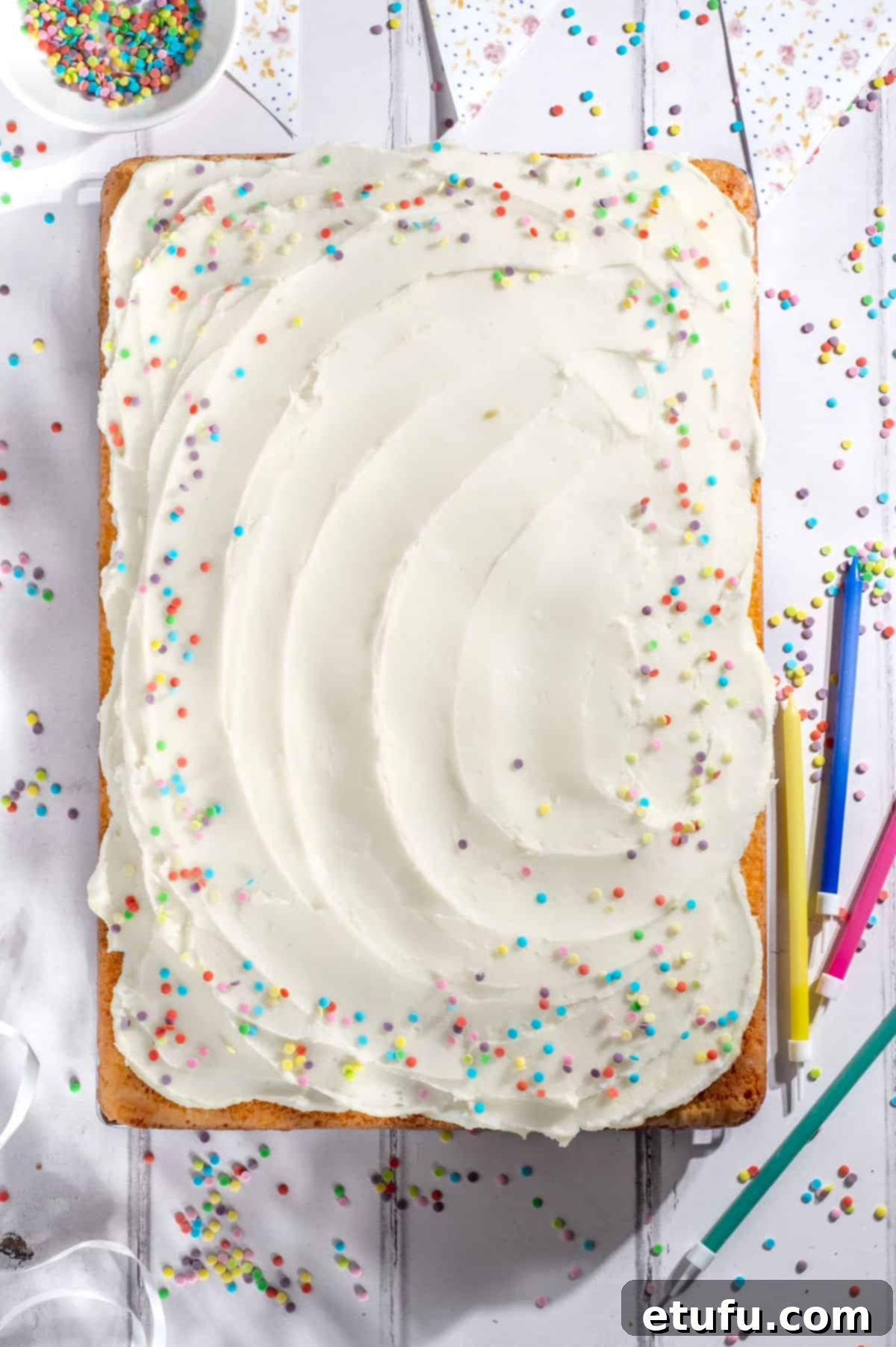 A vanilla traybake with sprinkles on a white background, highlighting its fluffy texture.