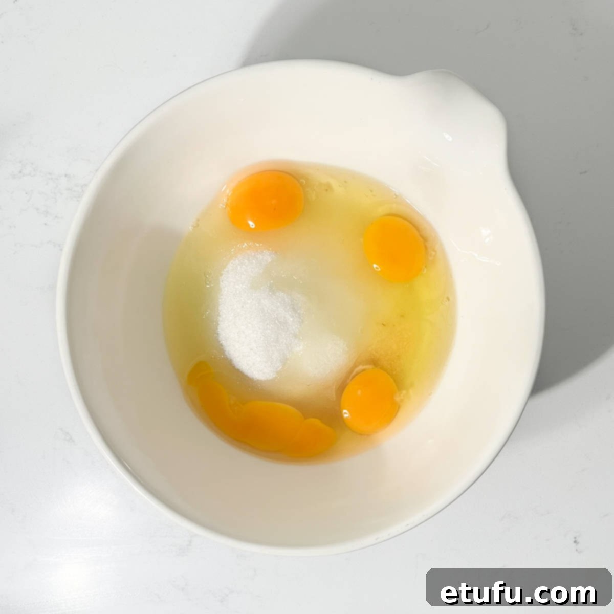 Adding granulated sugar, room-temperature eggs, and vanilla extract to a large mixing bowl.