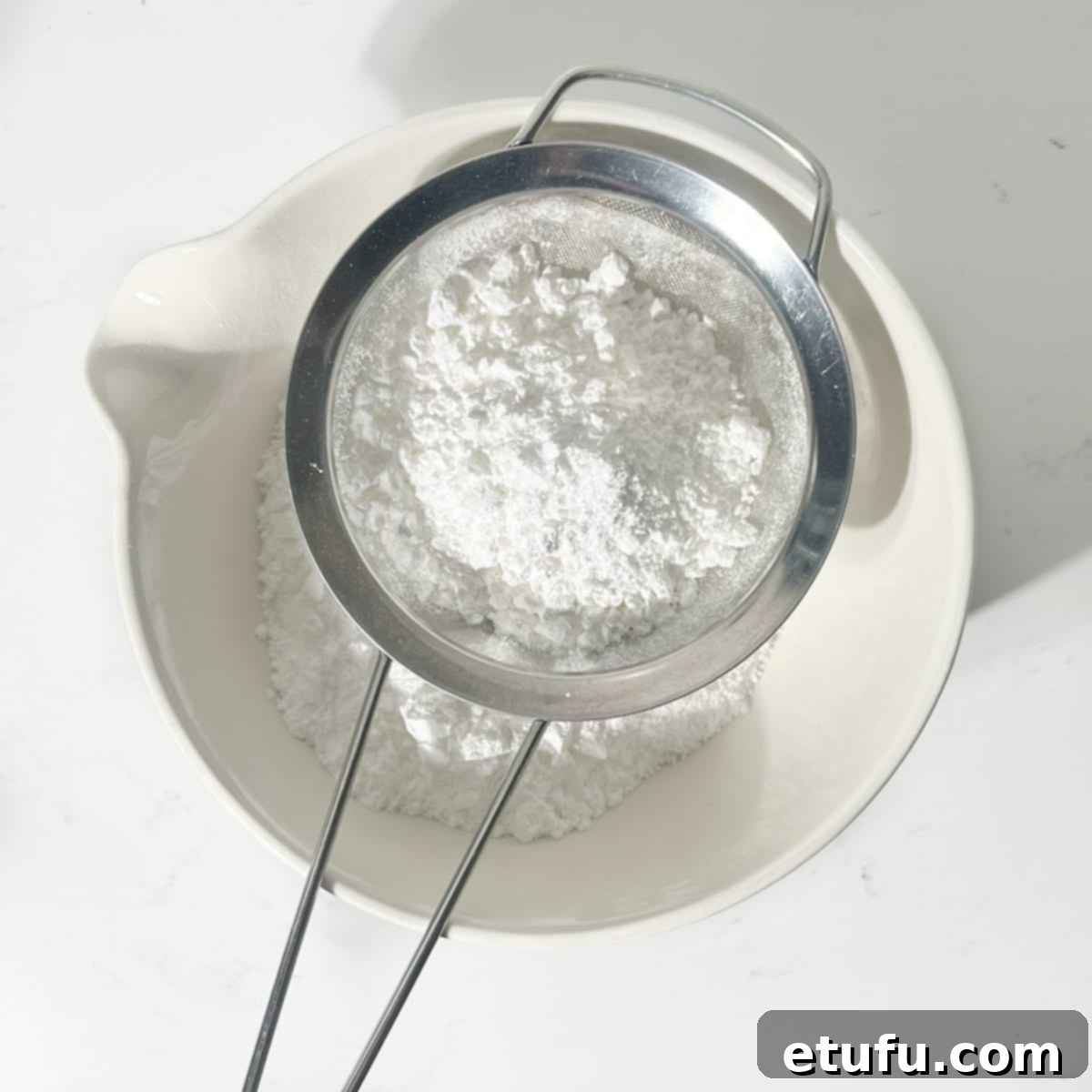 Sifting icing sugar and salt into a large bowl for vanilla buttercream.