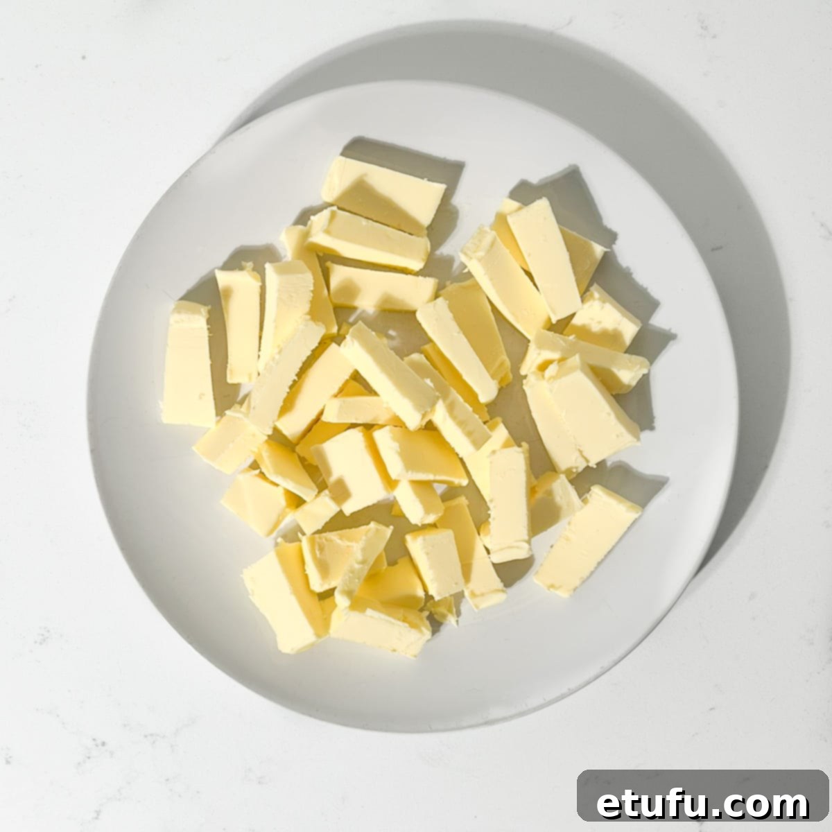Cubes of softened unsalted butter on a large white plate, ready for buttercream.