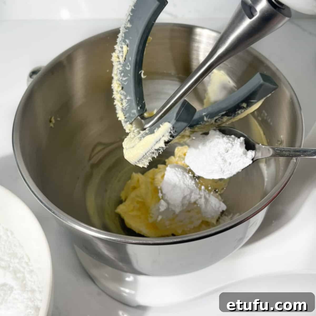 Gradually adding spoonfuls of sifted icing sugar to the whipped butter in a stand mixer.