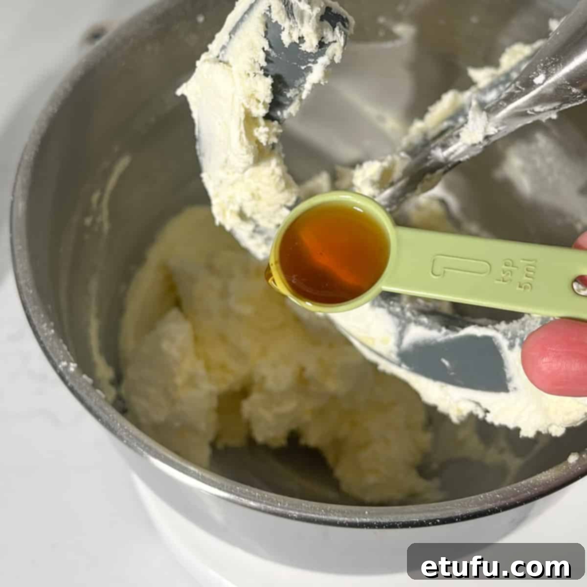 Adding vanilla extract to the finished buttercream in a stand mixer.