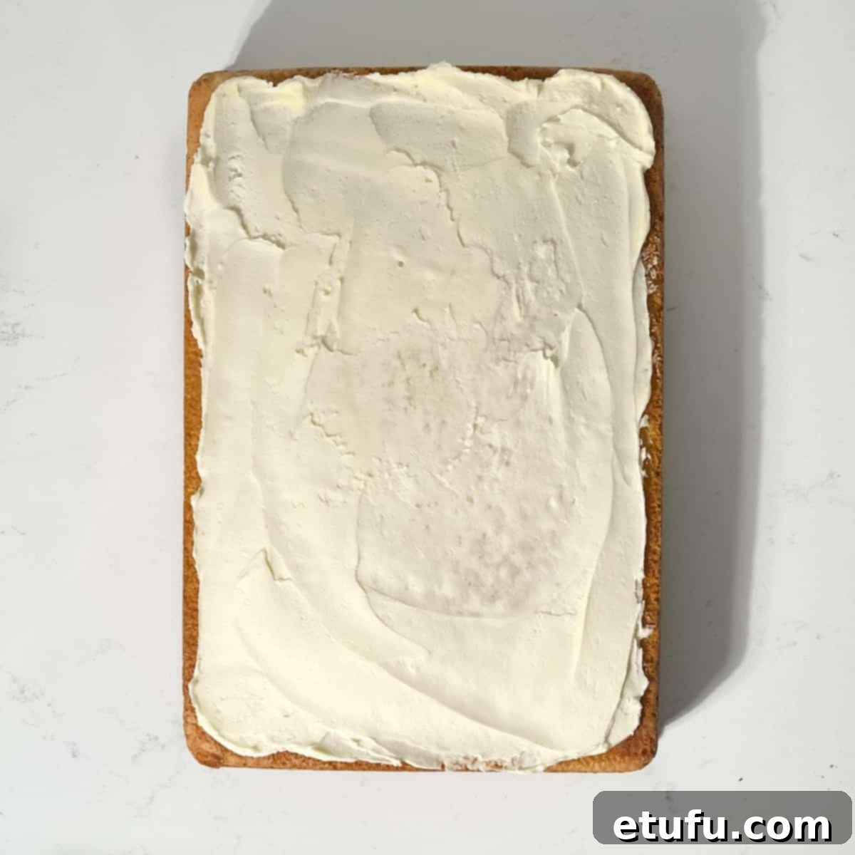 Spreading a thin crumb coat of buttercream over the cooled sheet cake with an offset spatula.