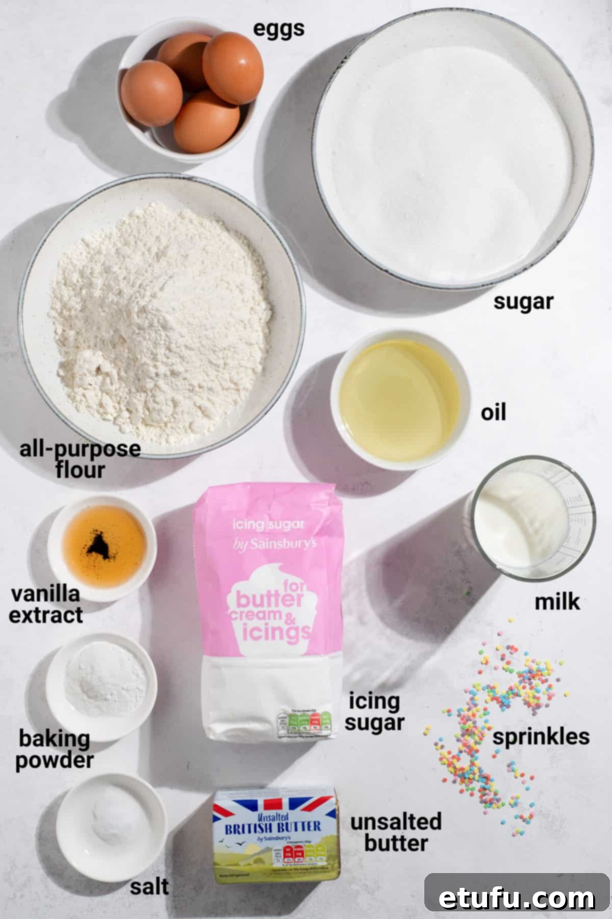 Various ingredients for vanilla tray bake, including eggs, flour, sugar, oil, and milk, laid out on a table.