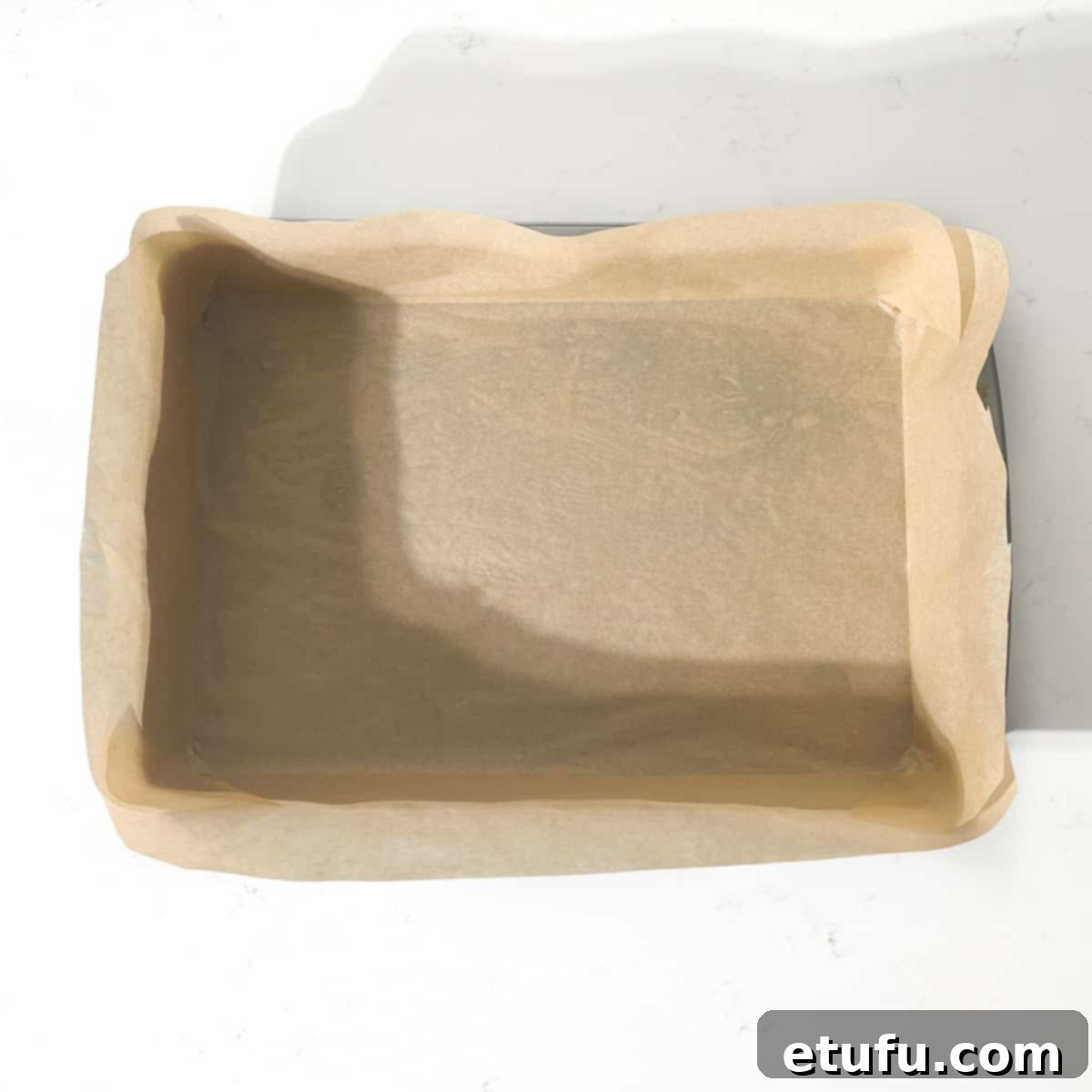 A baking tin neatly lined with baking paper, showing folded corners.