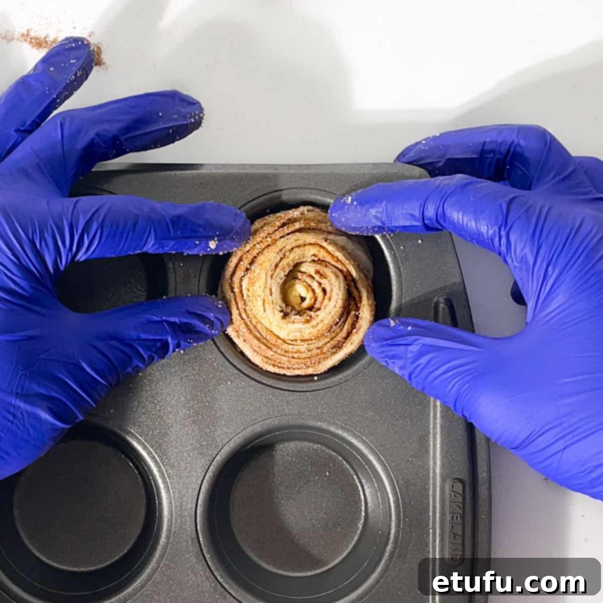 Placing one cruffin roll into the hole of a muffin tin.