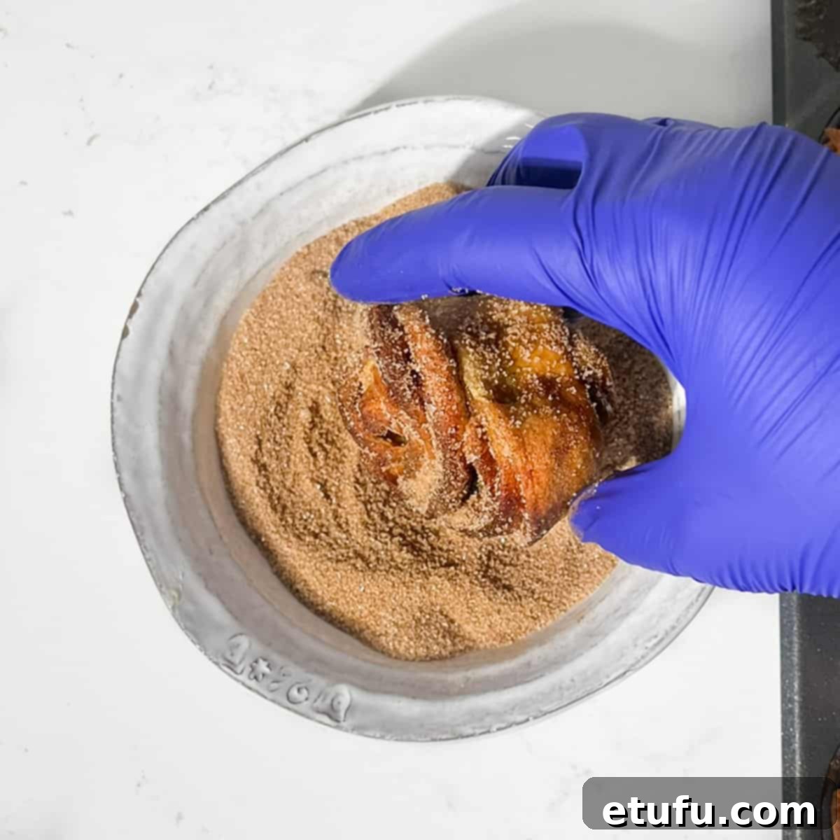 Rolling a cruffin in cinnamon sugar.