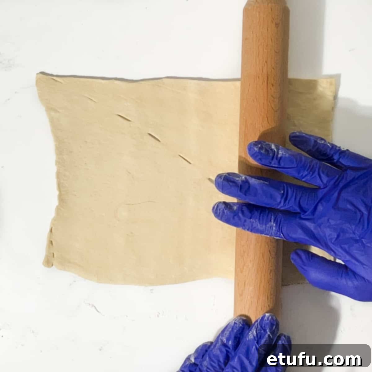 Rolling a square of crescent dough slightly larger with a rolling pin.