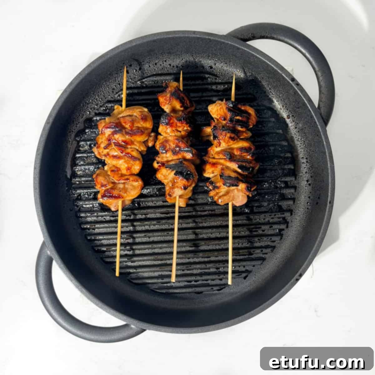 Chinese chicken on a stick grilling in a griddle pan.