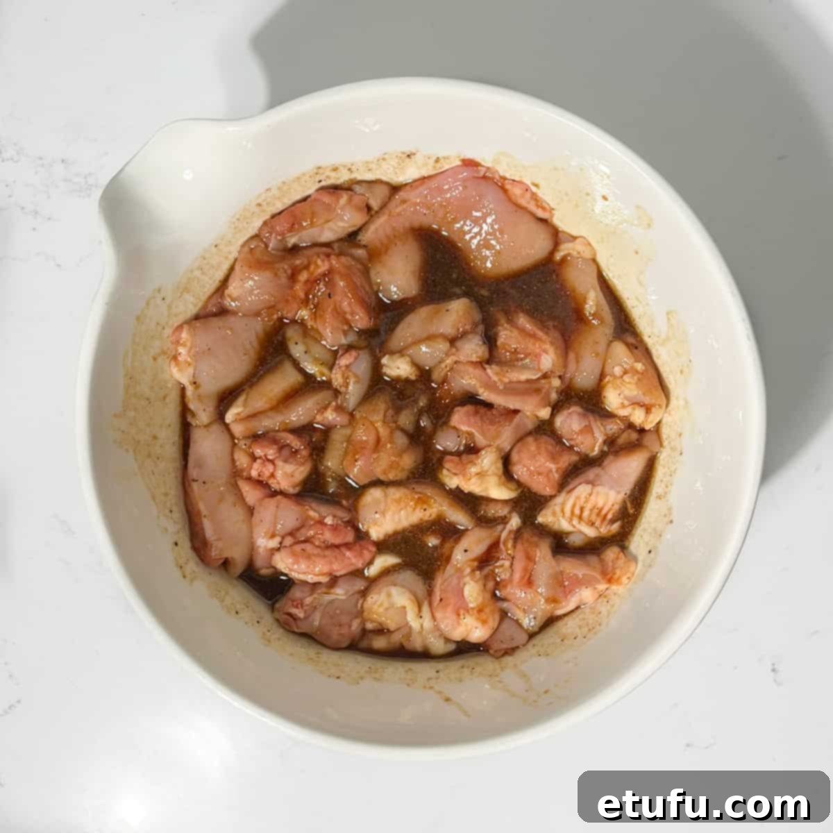 Teriyaki chicken marinating in a large white bowl.