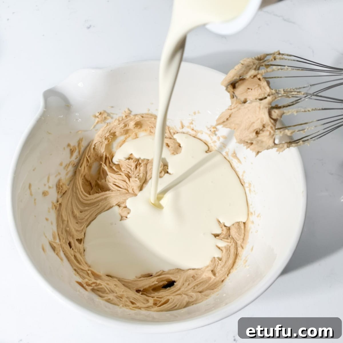 Adding cream to the mascarpone in a large white bowl.