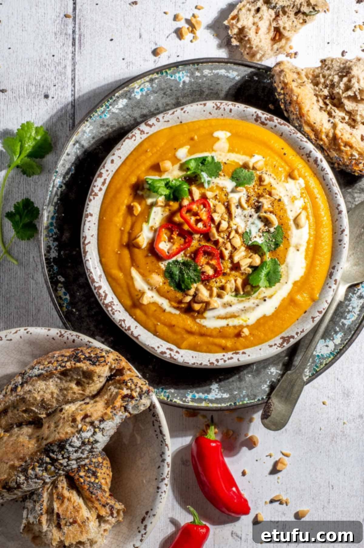 Sweet potato coconut and chilli soup in a soup bowl with a bowl of bread rolls on the side.