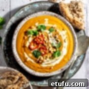 Sweet potato coconut and chilli soup in a soup bowl with a bowl of bread rolls on the side.
