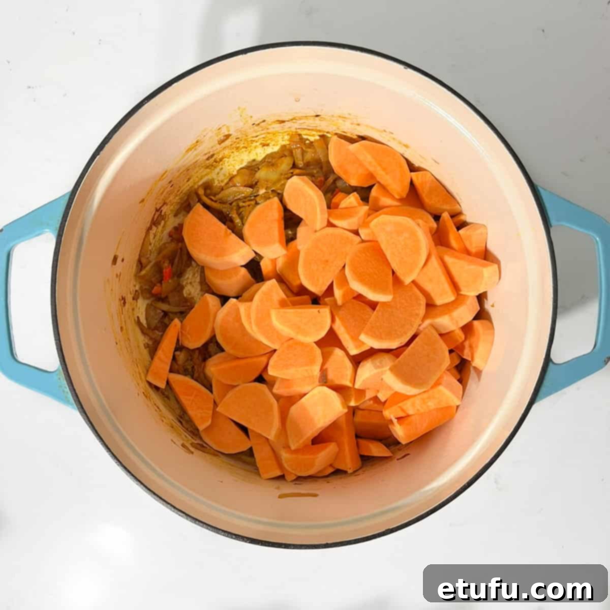 Adding sweet potato chunks top the caramelised onions in a large saucepan.