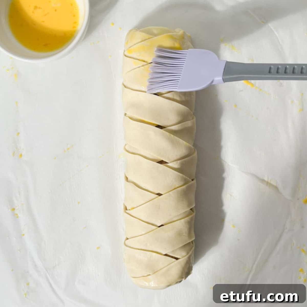Brushing the sausage plait with egg wash with a pastry brush.