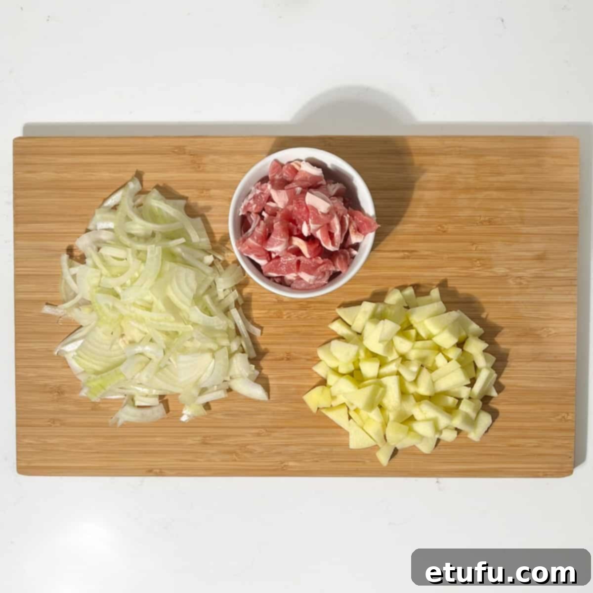 Chopped onions, apples and bacon on a wooden chopping board.