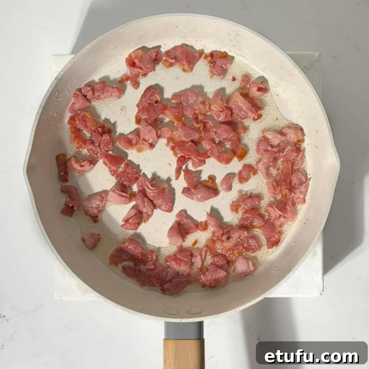 Bacon frying in a large frying pan.