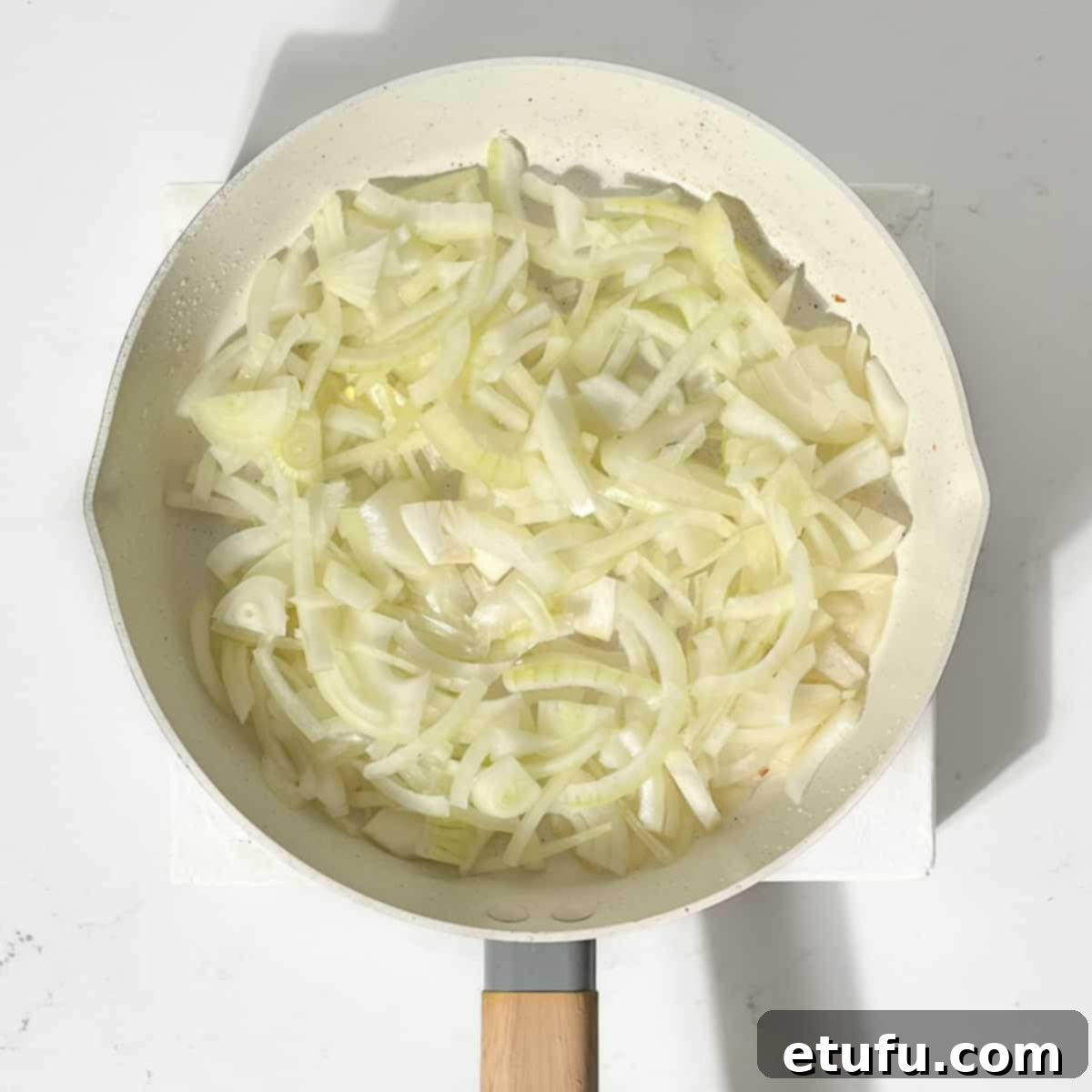 Sliced onions frying in a large frying pan.