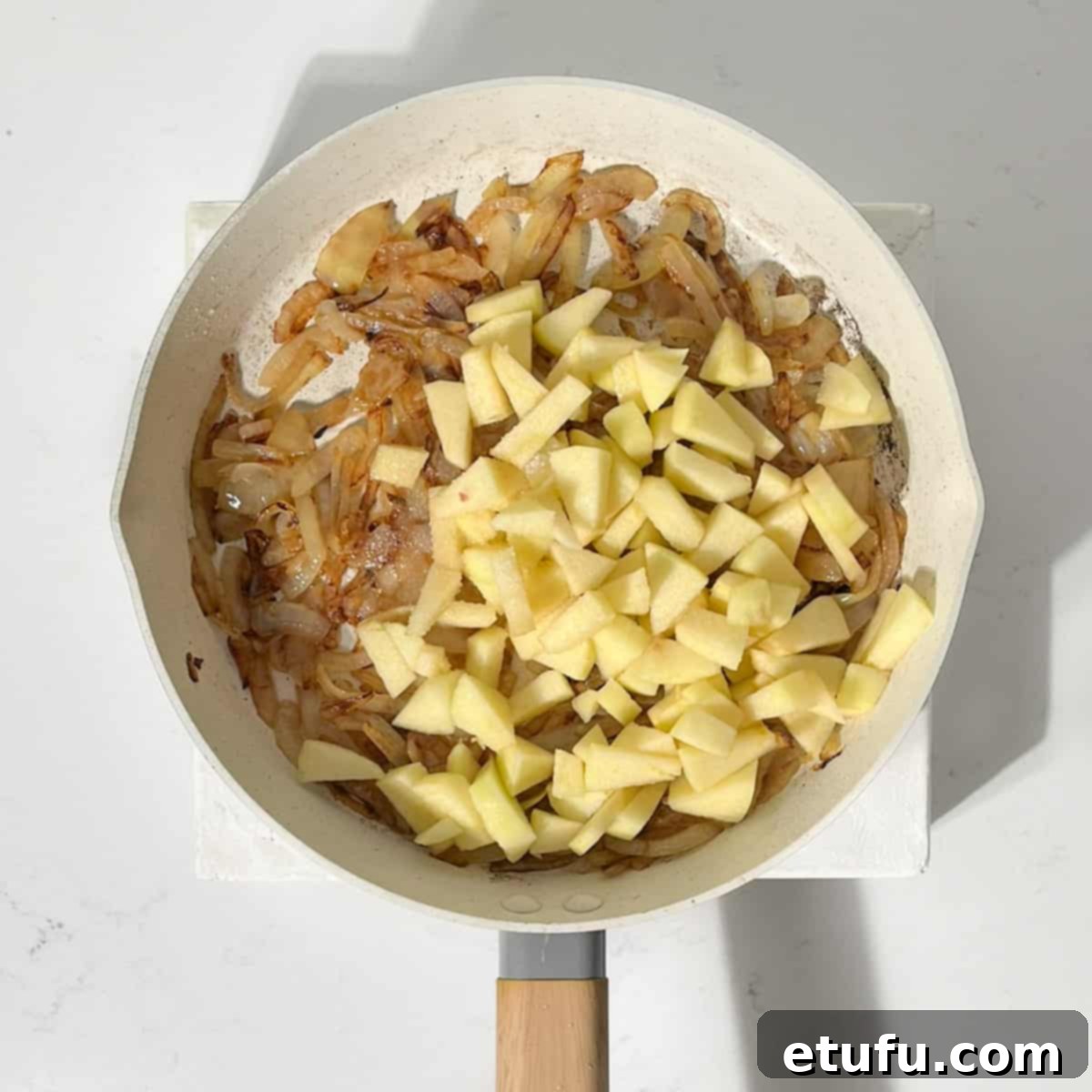 Apples and onions cooking in a frying pan.