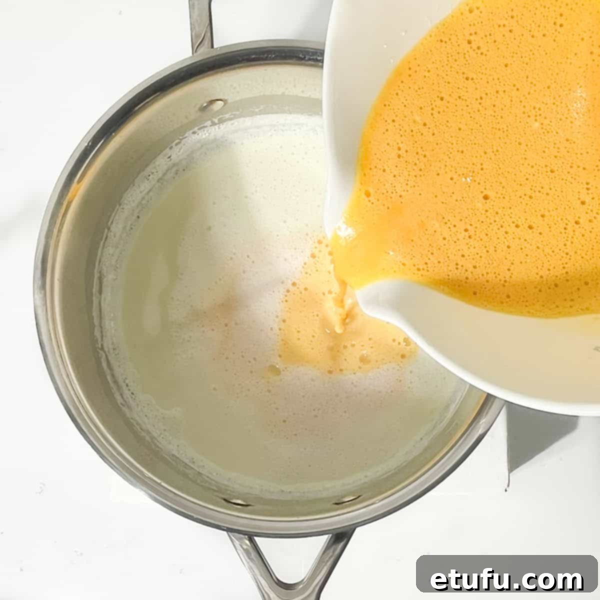 Pouring the egg mixture into the warm milk in the saucepan.