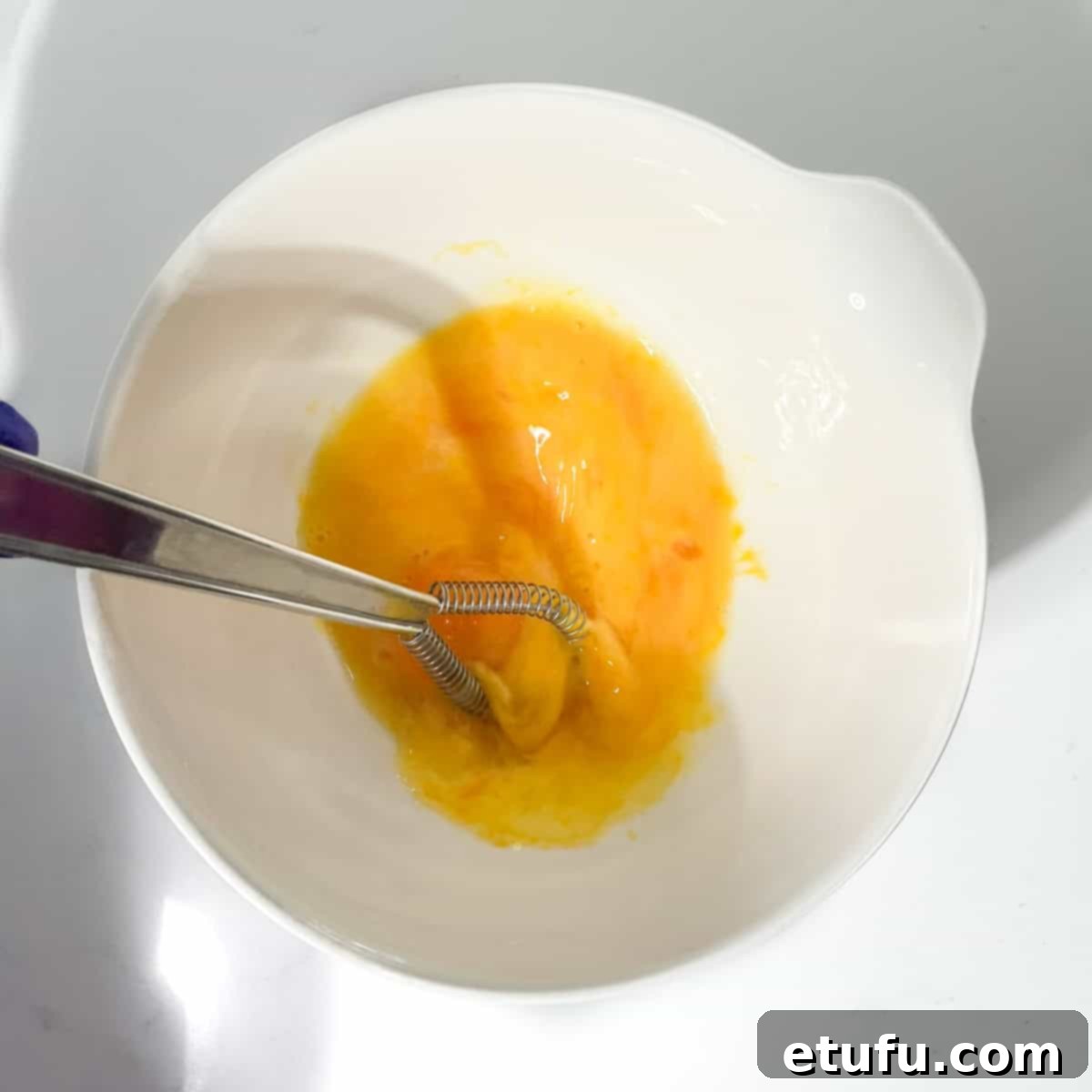 Whisking egg yolks and water in a white mixing bowl.