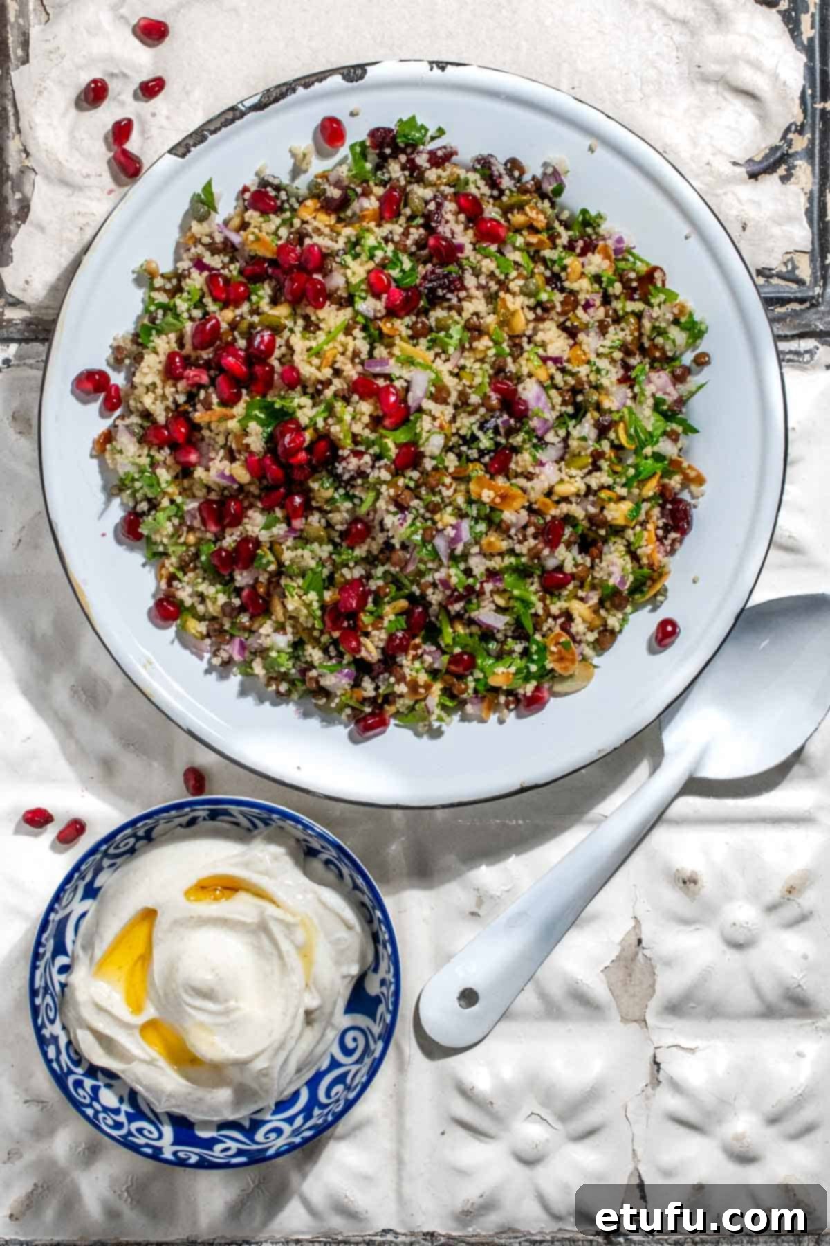 Cypriot grain salad on old white metal tiles with a bowl of Greek yoghurt dressing.