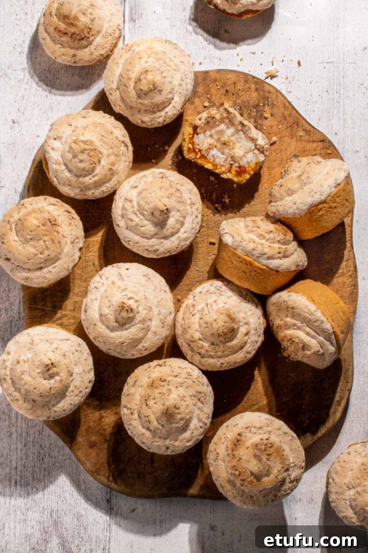 Hertzoggies on a wooden board on a white background, showcasing their golden meringue tops and delicate pastry.