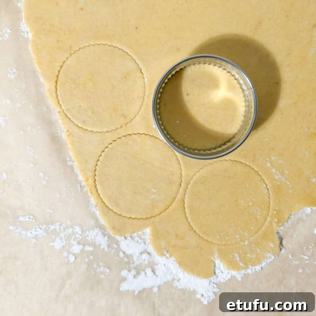 Pastry dough being cut into circles with a cookie cutter, prepared for lining the tartlet pans.