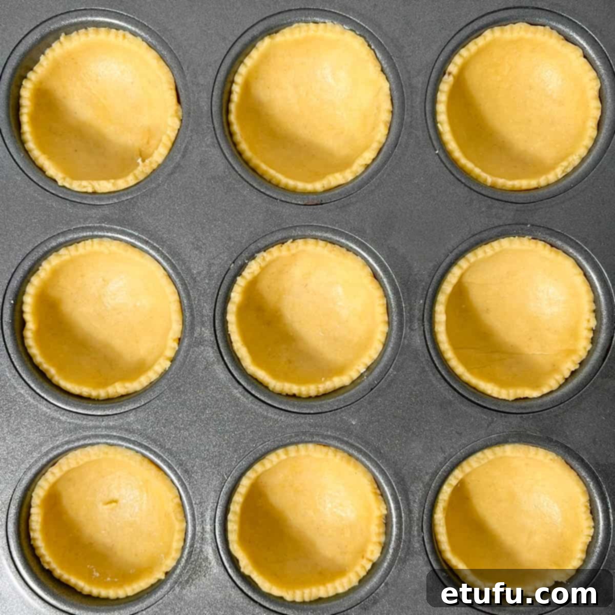 Pastry cases carefully lined in a muffin tray, ready for the apricot jam filling.