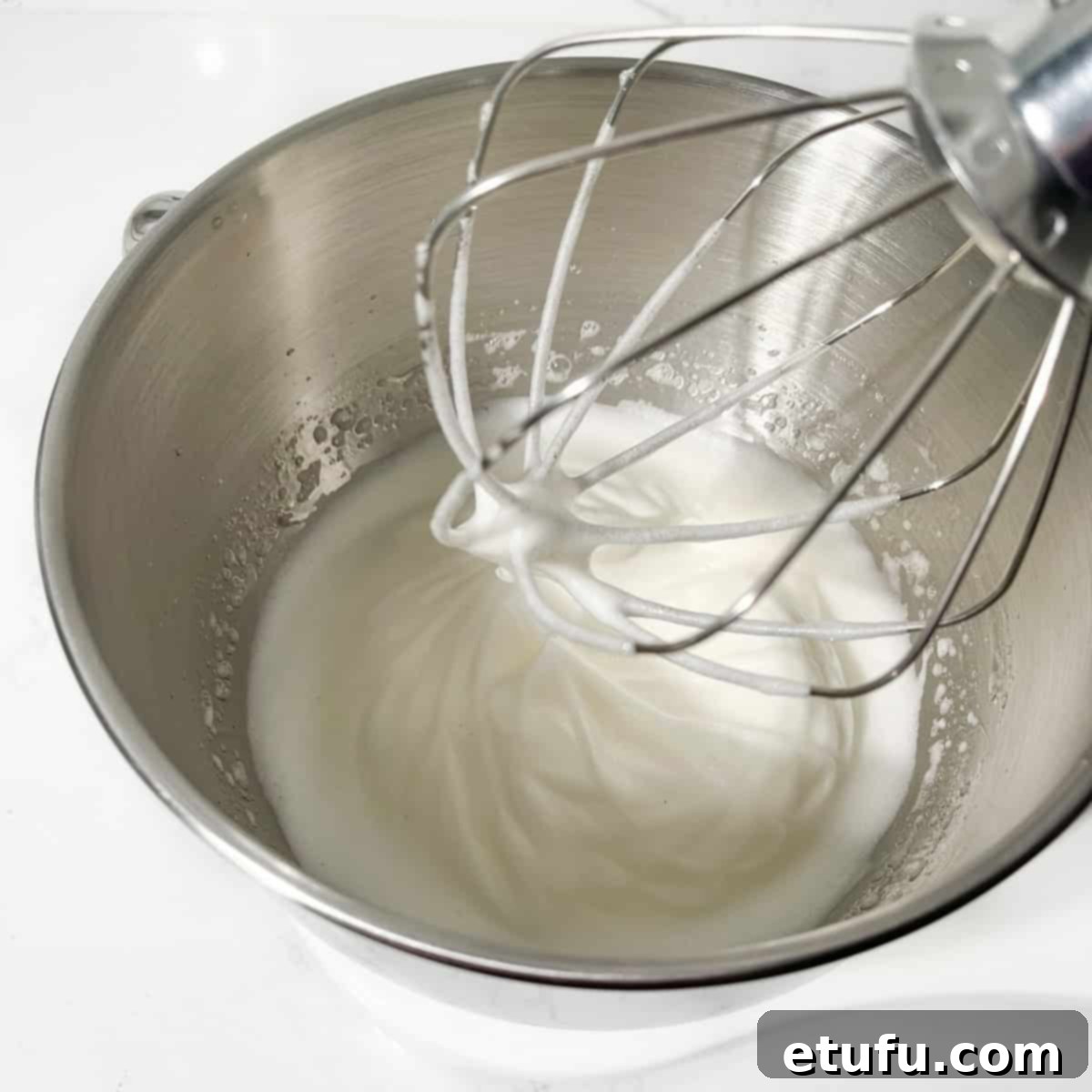 Stiff peaks formed from whipped egg whites in a stand mixer bowl, indicating the perfect consistency for meringue.