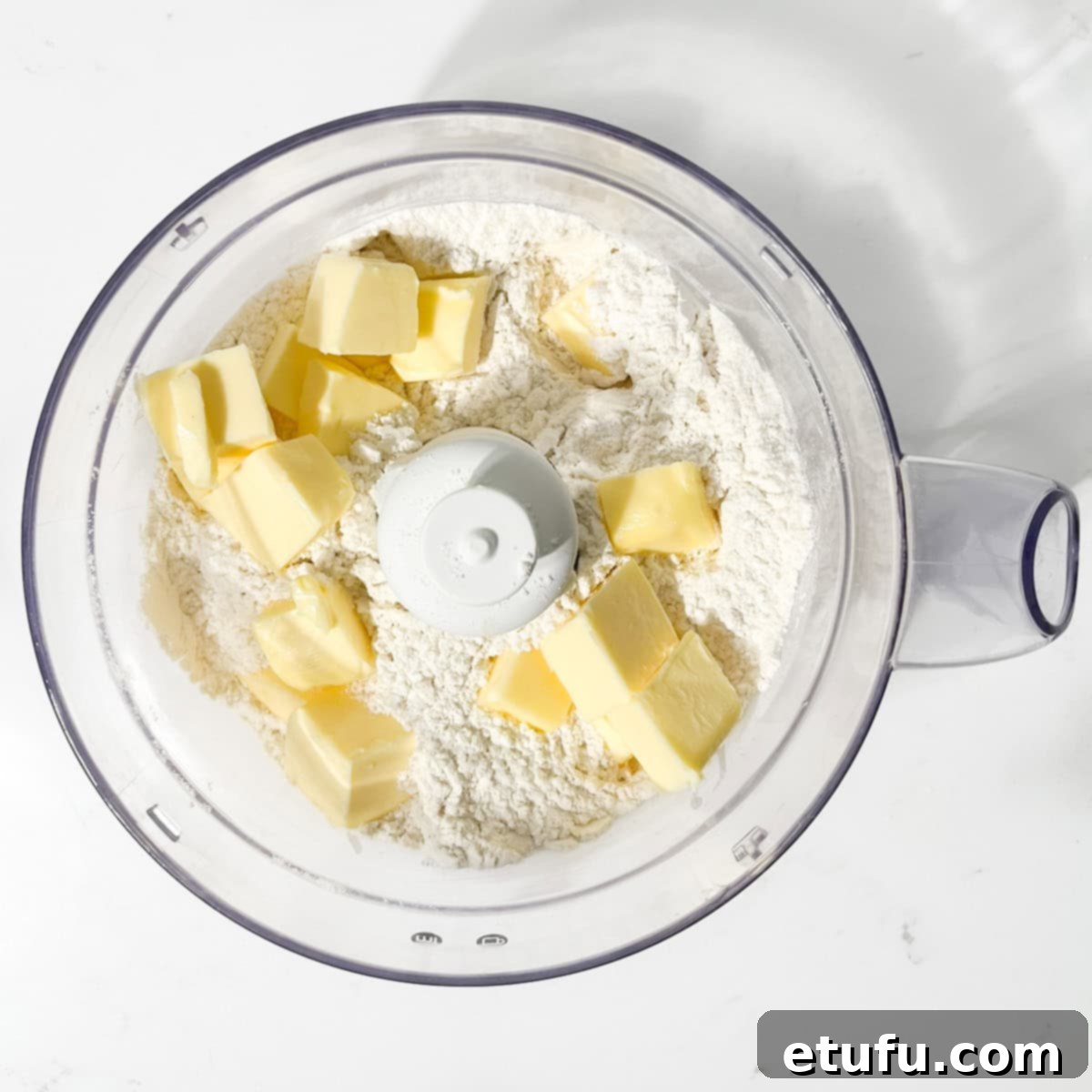 Cubed room-temperature butter being added to the sifted dry ingredients in a food processor for Hertzoggies pastry.