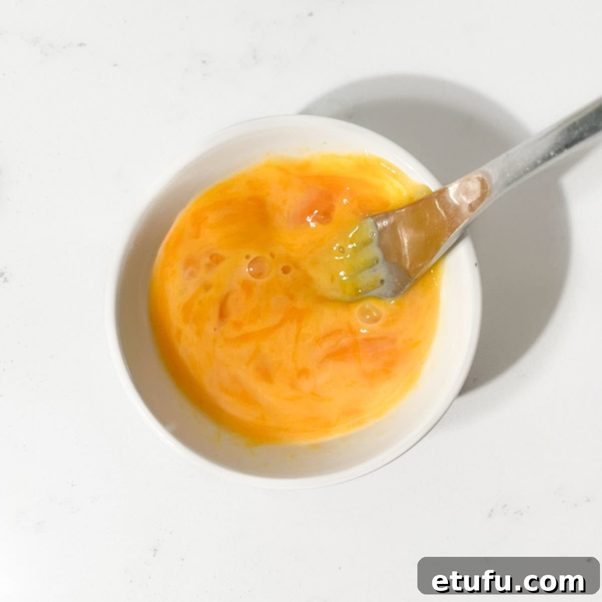Egg yolks being whisked with cold water in a small white bowl, preparing to be added to the pastry dough.