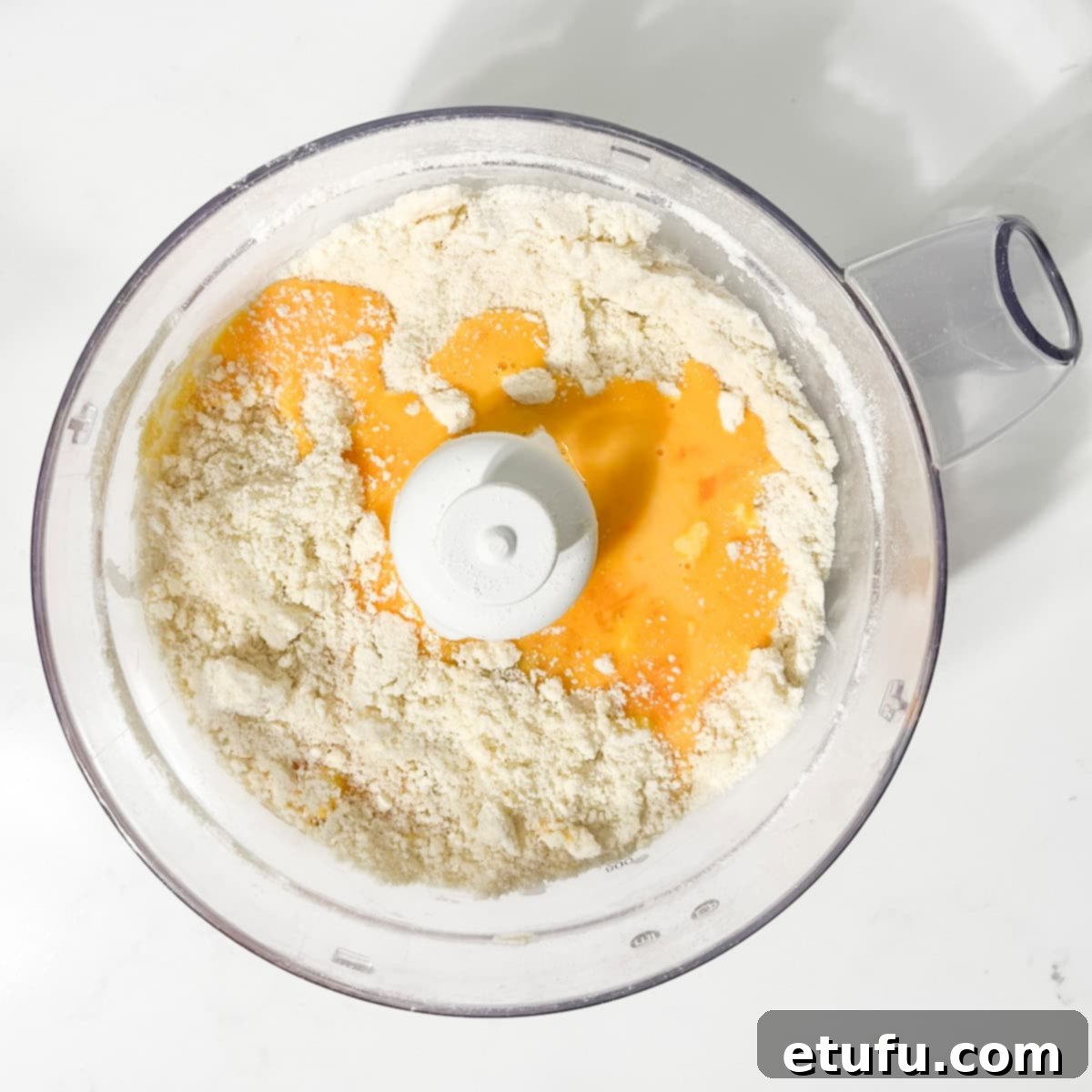 The whisked egg yolk and cold water mixture being added to the butter and flour mixture in the food processor.