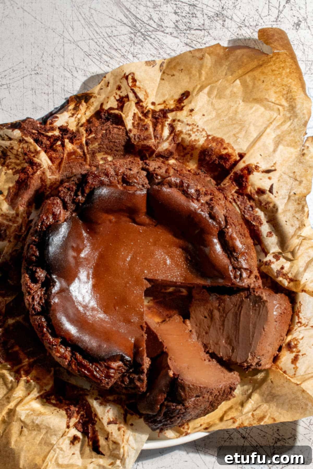 A chocolate basque cheesecake in the baking paper it was baked in with two slices cut from it. 