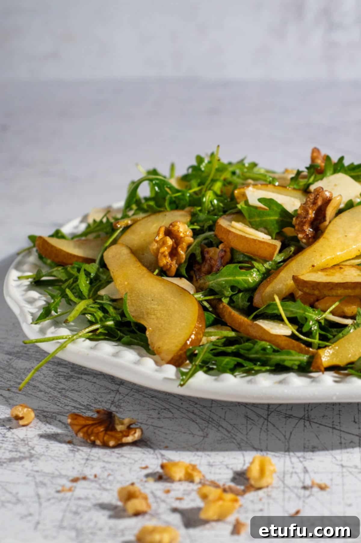 Pear and rocket salad on a large white plate, garnished with fresh herbs.