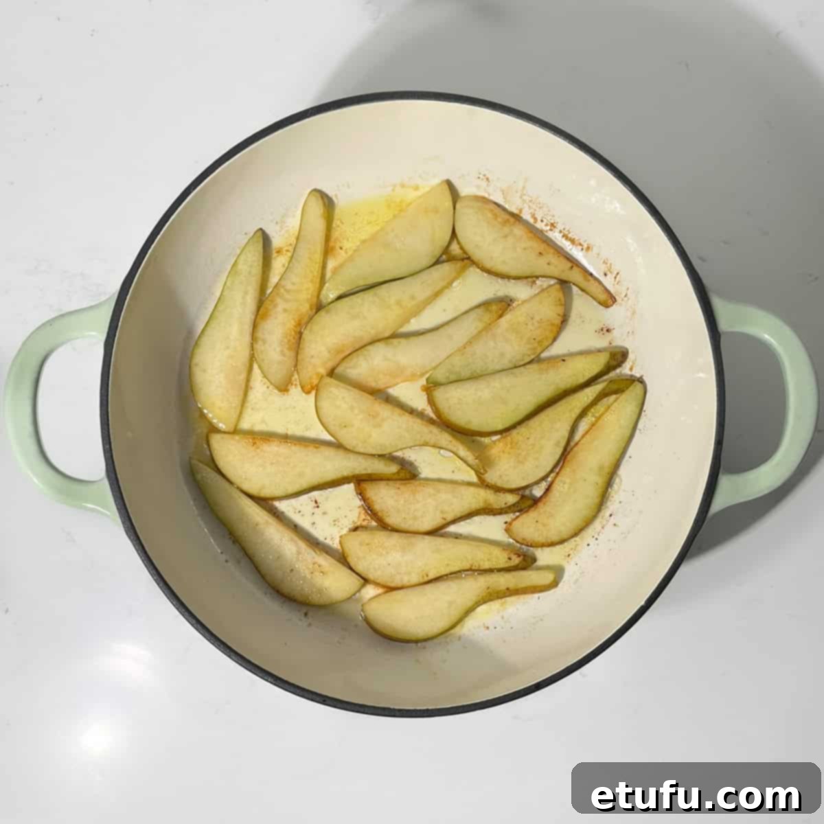 Pears caramelizing to a light golden color in a large frying pan.