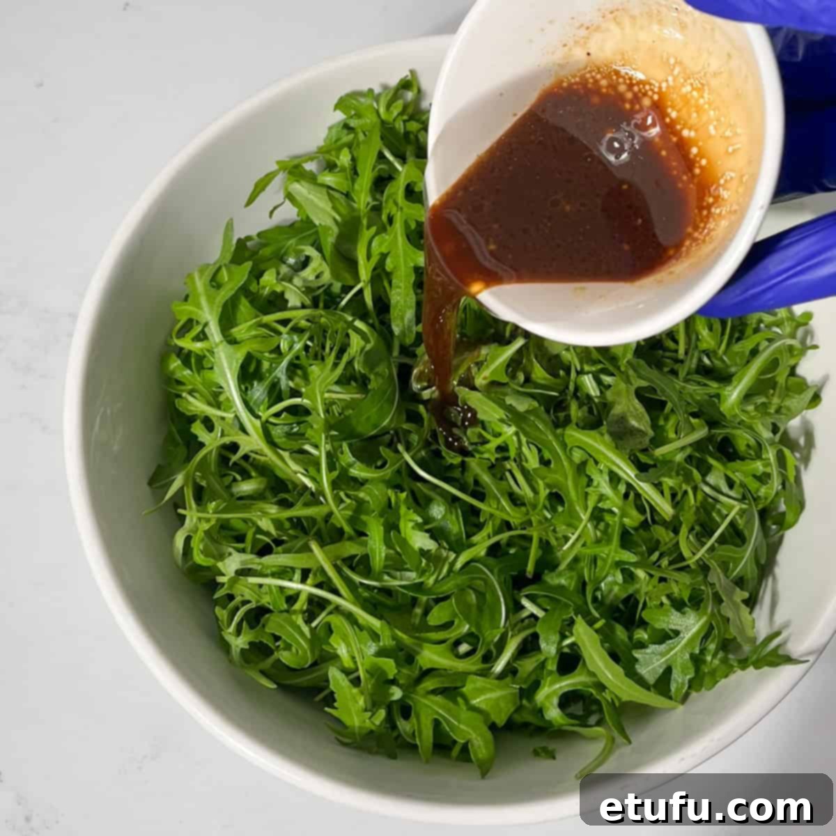 Drizzling the prepared dressing over fresh rocket (arugula) leaves in a large bowl.