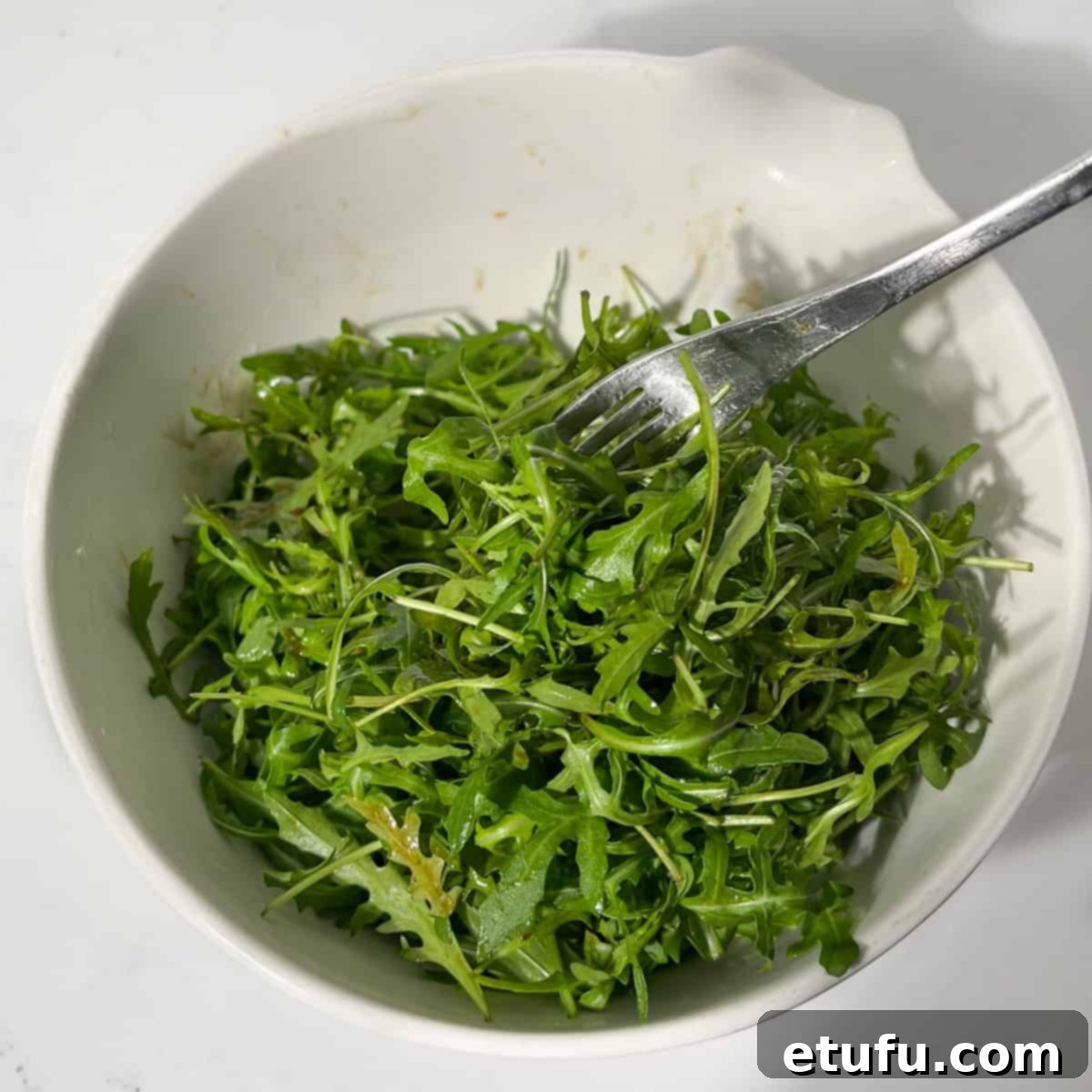 Gently mixing the dressing with rocket leaves using two forks in a large white bowl.