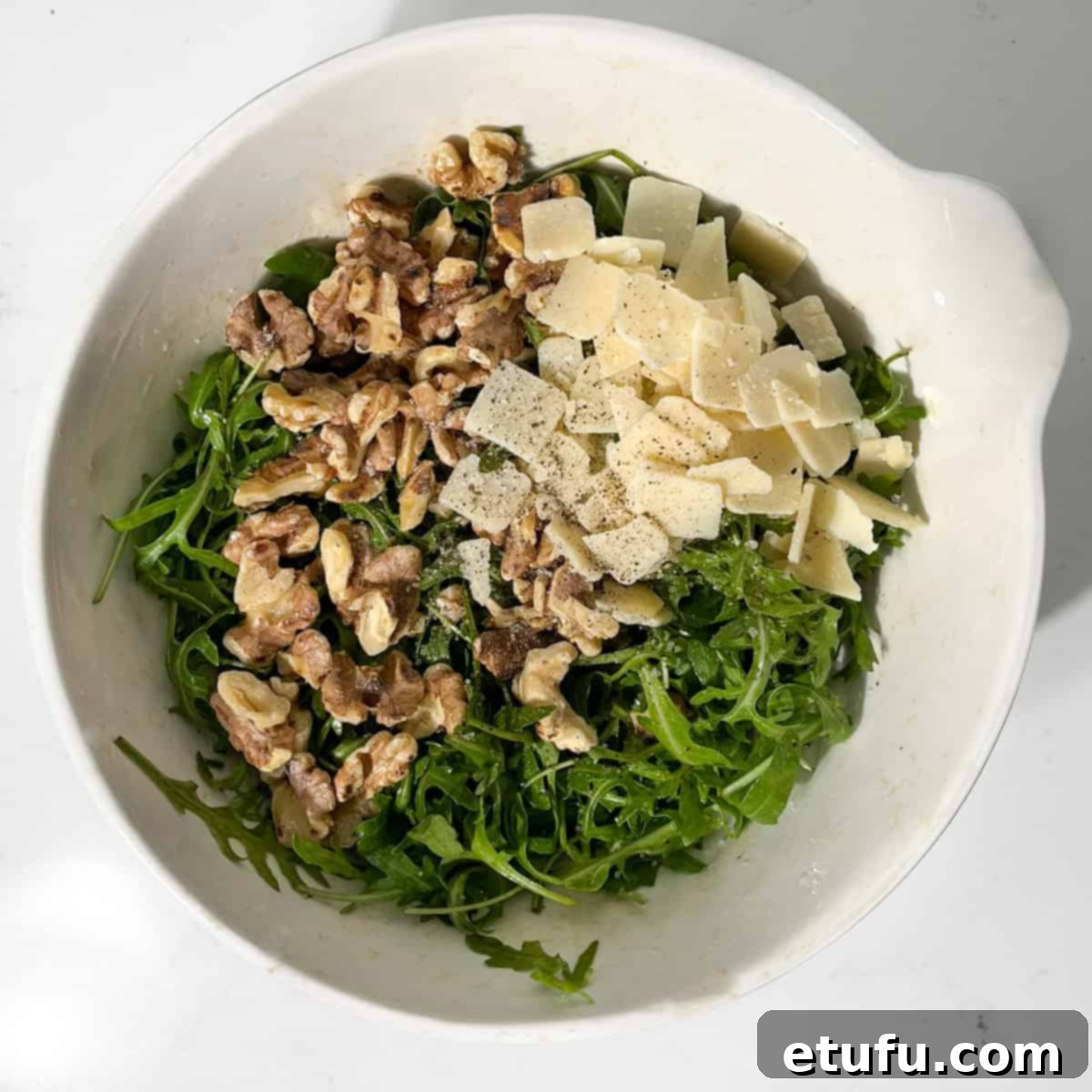 Adding parmesan shavings and toasted walnuts to the dressed rocket leaves.