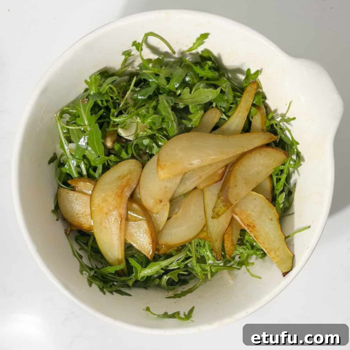 Gently adding the cooled caramelized pear slices to the assembled pear and rocket salad.