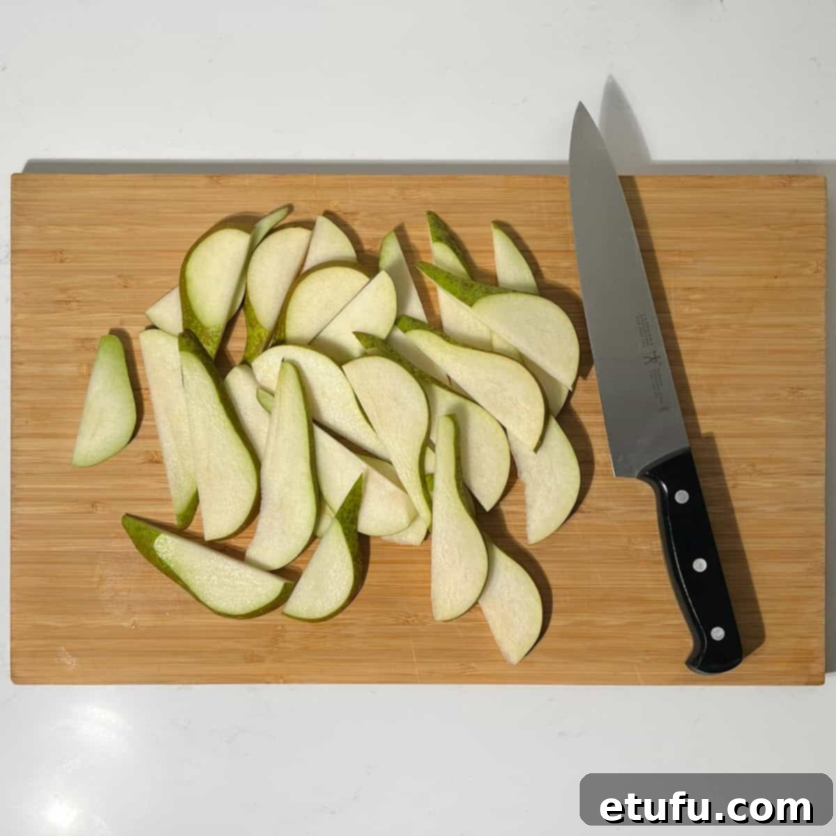 Slicing pears into thin, uniform pieces on a wooden cutting board.