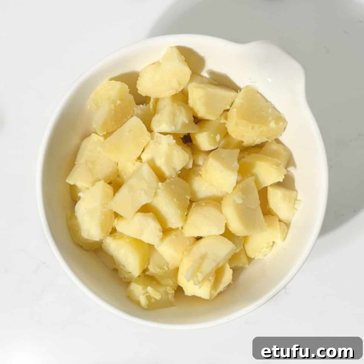 Cooked potato cubes in a large white bowl.