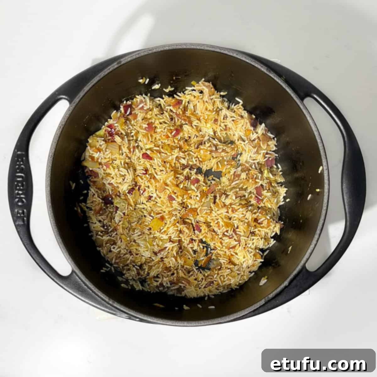Sultan's Moroccan Pilaf 7 Stirring thoroughly rinsed basmati rice into the fragrant mixture of bloomed spices and sautéed onions in a black saucepan.