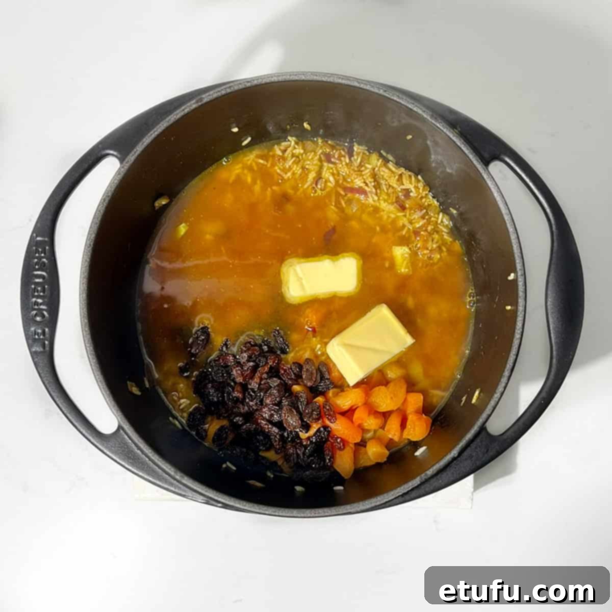Sultan's Moroccan Pilaf 8 Pouring hot vegetable stock into the saucepan with toasted rice and spices, alongside butter, salt, raisins, and dried apricots.