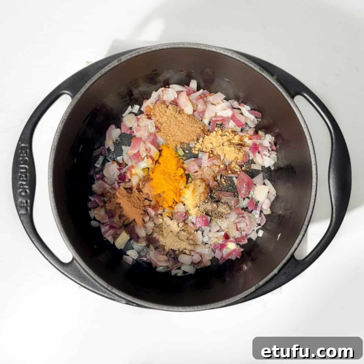 Sultan's Moroccan Pilaf 6 Adding a vibrant array of ground spices—coriander, turmeric, cinnamon, cardamom, ginger, pepper, and cloves—to softened onions in a black cast iron saucepan.